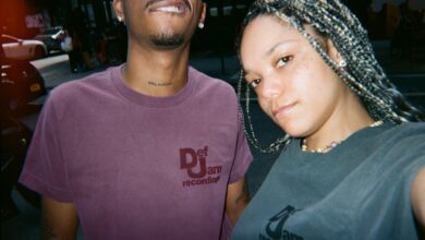 Two people taking a selfie, both wearing Def Jam Recordings shirts. The person on the right has braided hair.